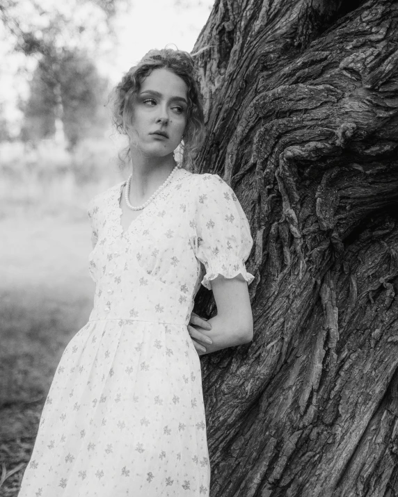 a woman leaning against a tree trunk in black and white