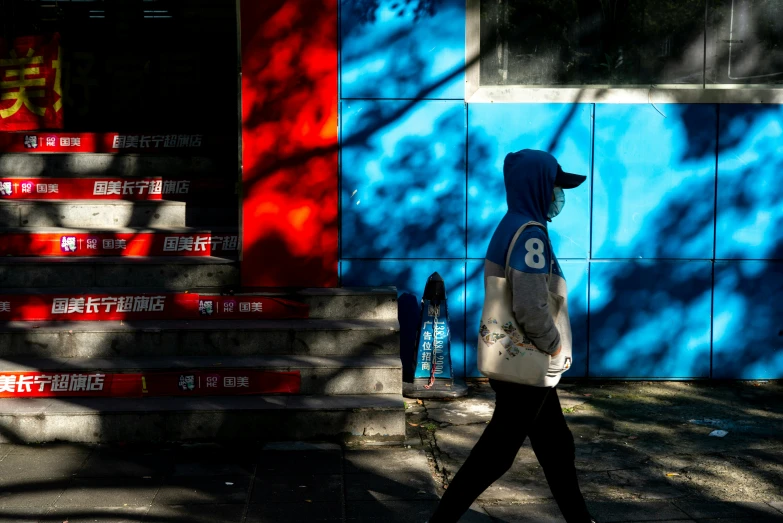 a person in a hooded jacket walking by a wall with steps painted blue and red