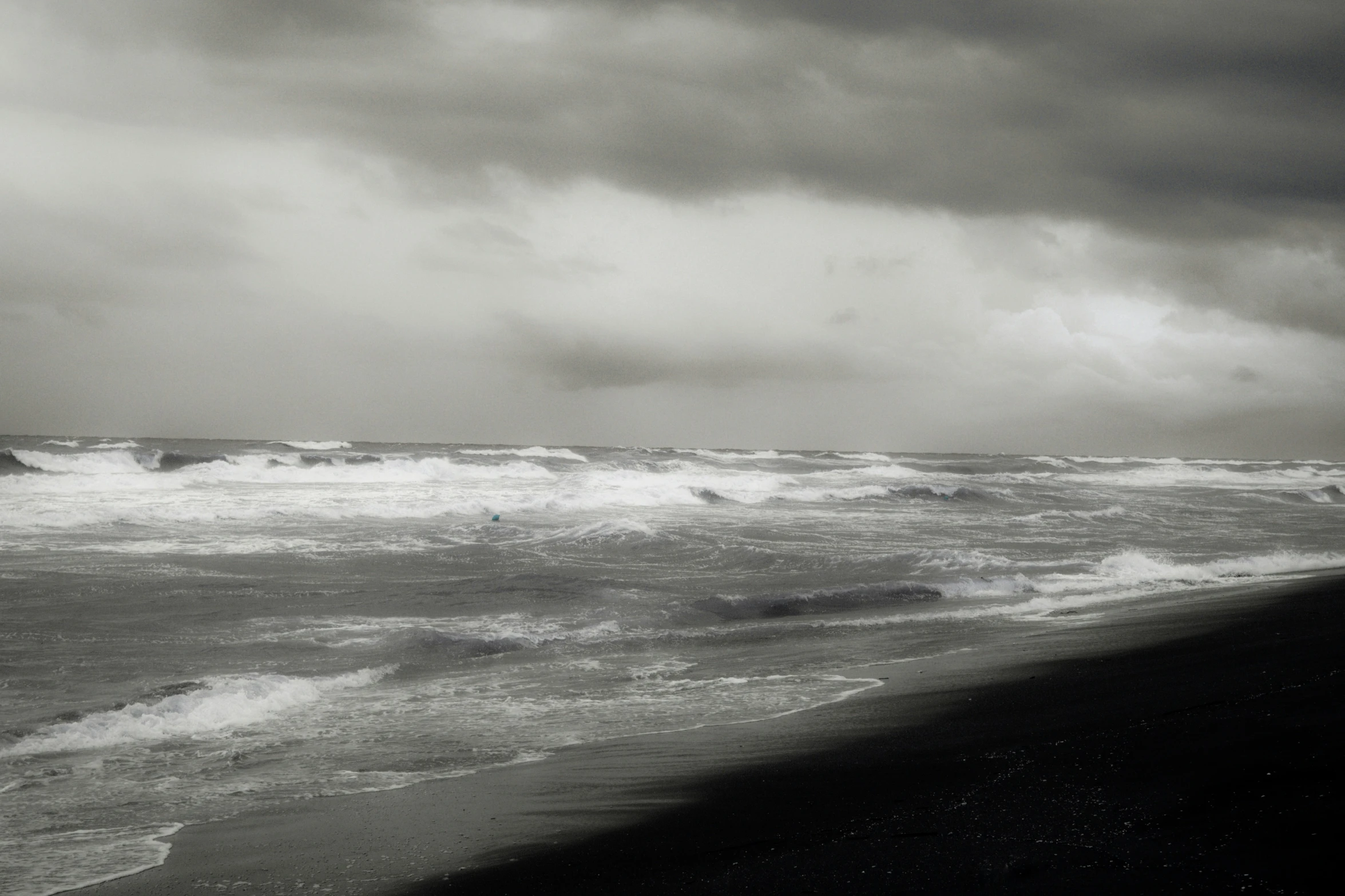 dark clouds cover the sky above some beach waves