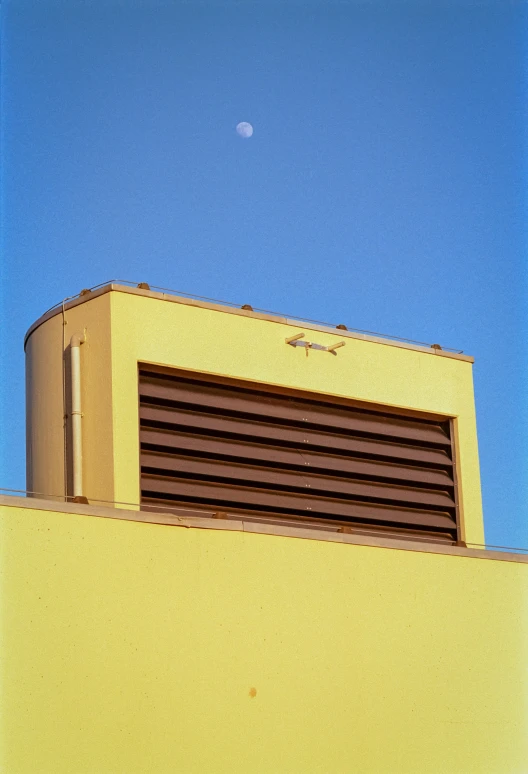 a yellow building with a half moon visible in the background