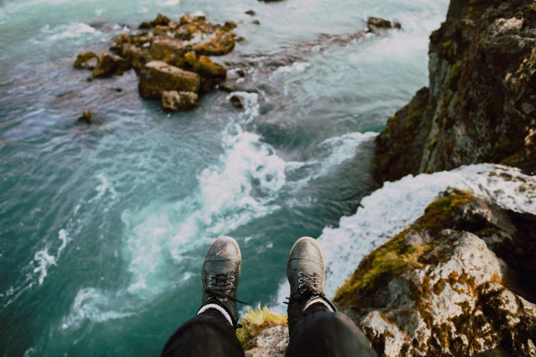 person with feet on rock standing on edge of cliff looking out at ocean