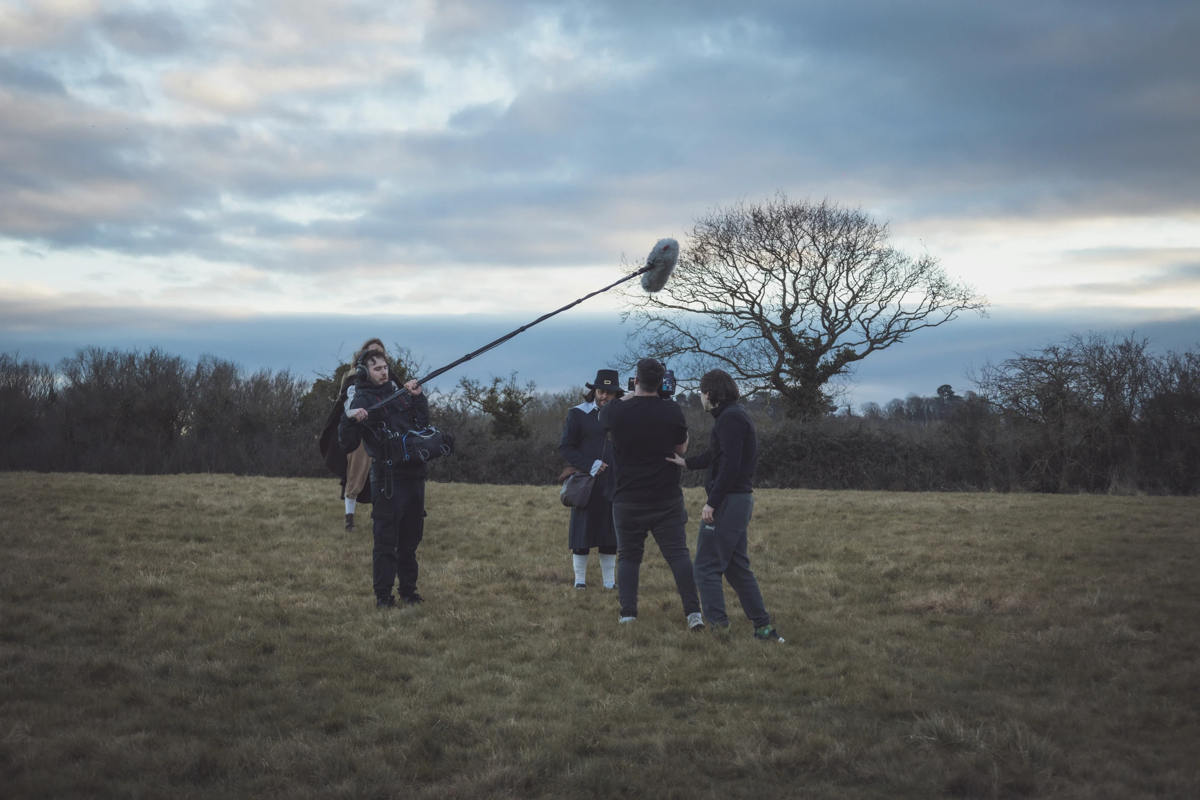 people in a field, the cameraman is holding the pole while holding up the ball and the other woman is holding the strings