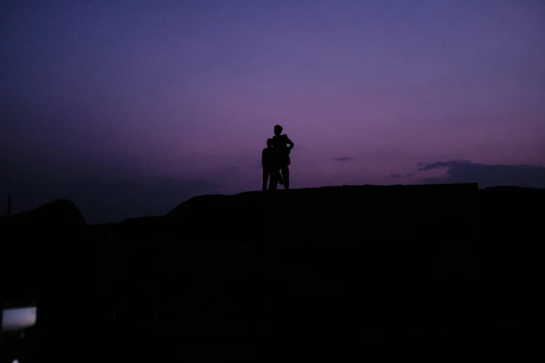 two people standing on top of a hill with the sky at night