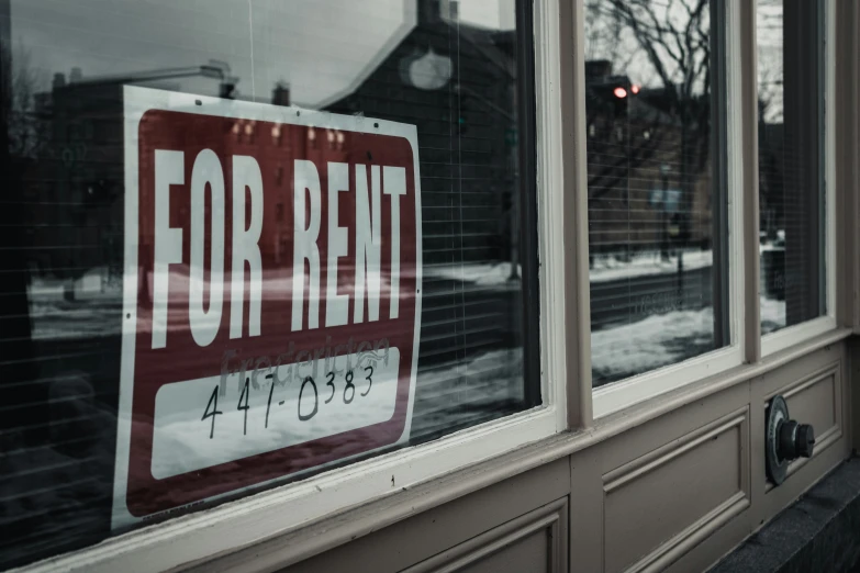 a red for rent sign sits behind the windows of an apartment