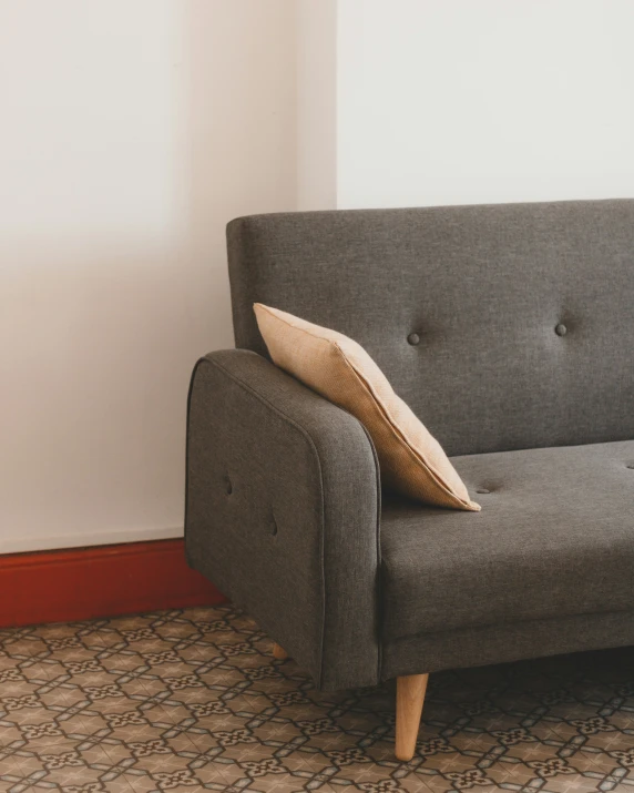 a grey couch with a wooden legs sitting in a corner