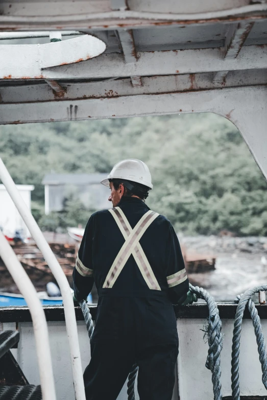 a man in overalls and helmet looking at soing while sitting on the deck of a boat