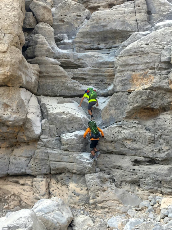 two people climbing over the edge of some rocks