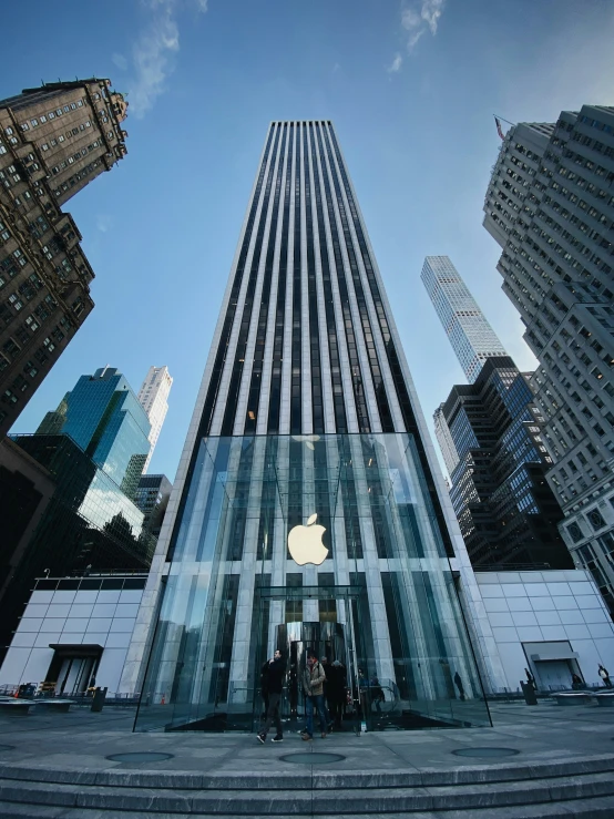 several people standing in front of an apple store with skyscrs in the background
