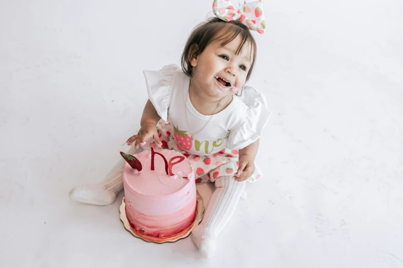 a little girl sitting on the ground with a pink cake and her name written in the cake