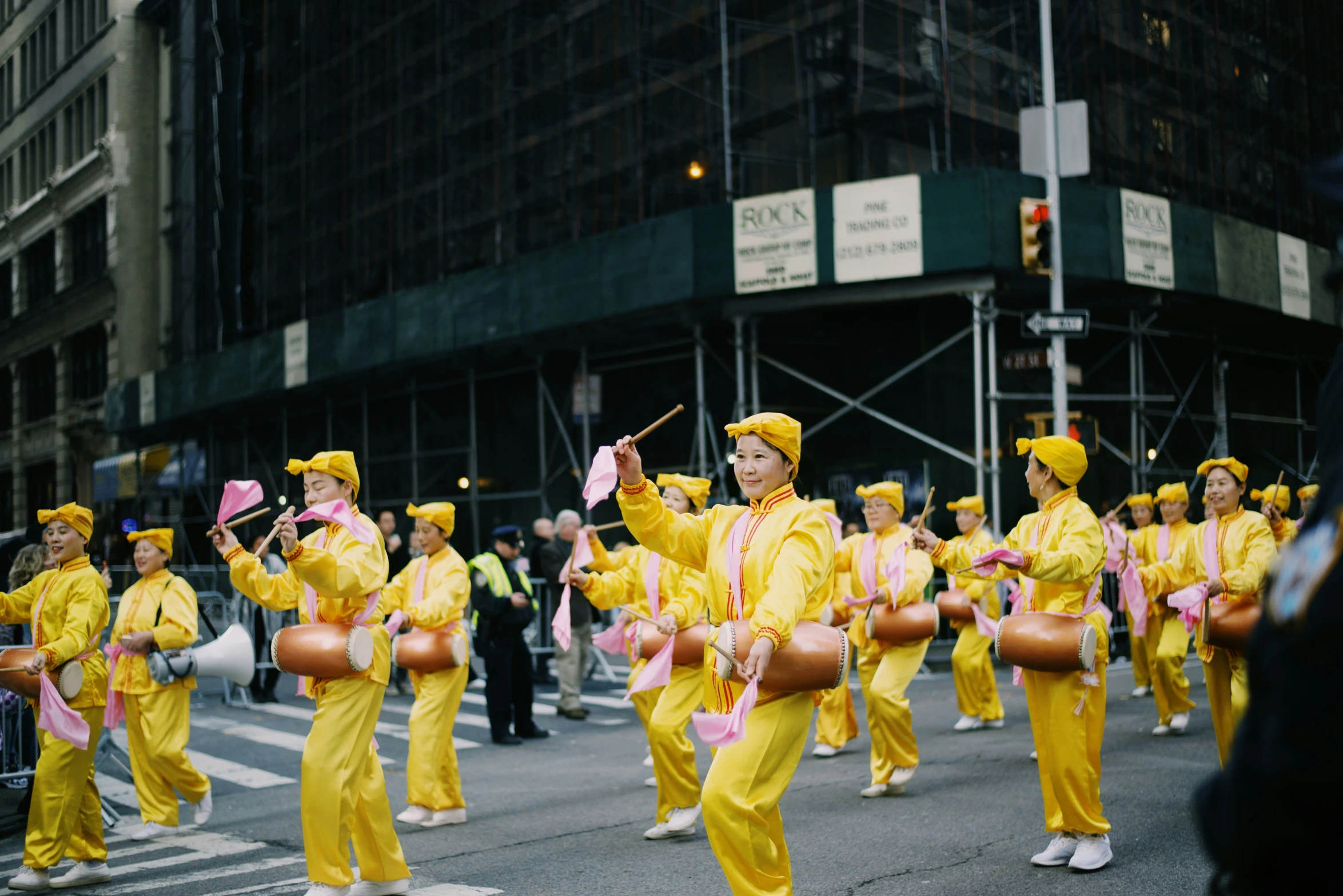 a group of men in yellow outfits carry metal drum as they walk in front of a crowd