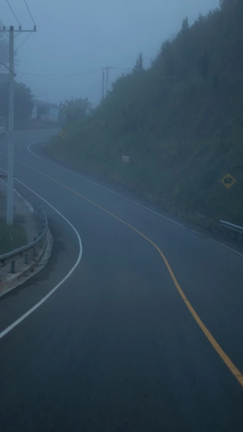 the road curves through a grassy hill and fog in the background
