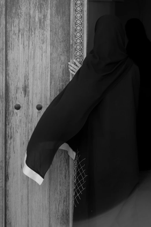a man in abaq standing at door way holding onto the door