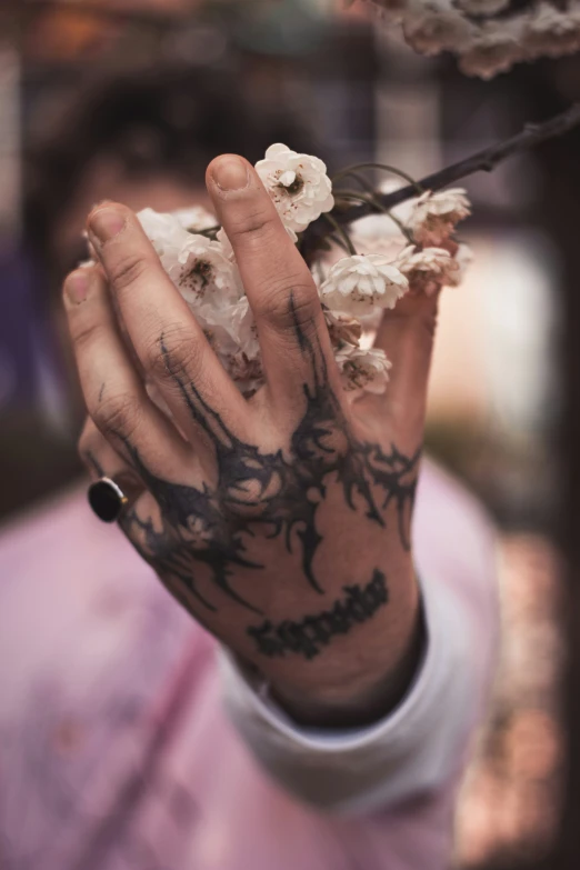 tattooed hand holding a nch with two white flowers