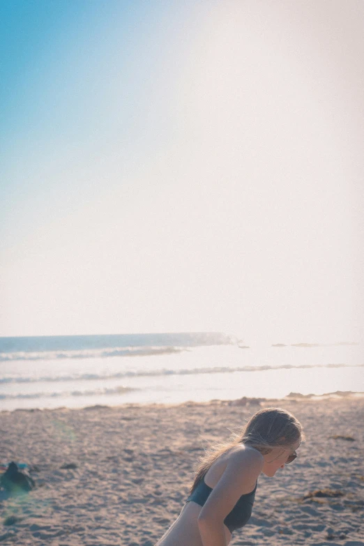 a woman kneeling down to a surfboard on a beach