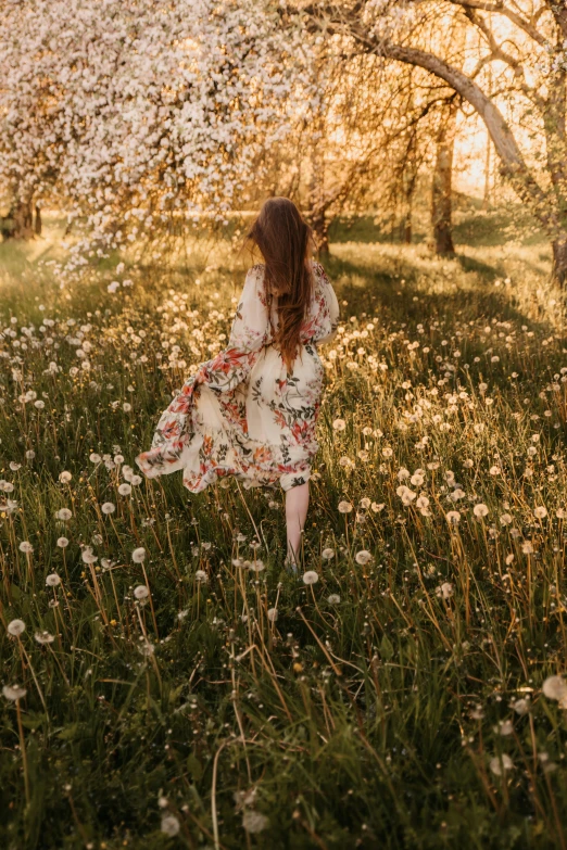 a young woman wearing a floral print dress walking through a field of dandelions