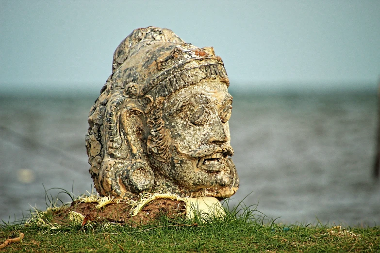 a stone statue of a buddha standing on a hill near the water