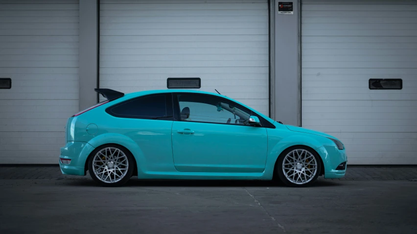 a turquoise hatchback car parked in front of a garage door