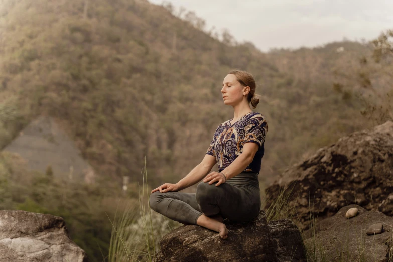 a woman sitting on top of a rock in a yoga position
