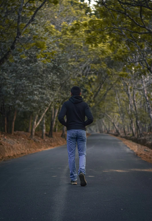 a man walks down the road wearing a black hoodie