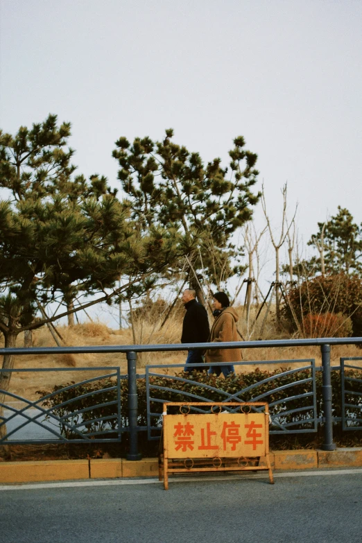 two people stand on a bridge near an open field