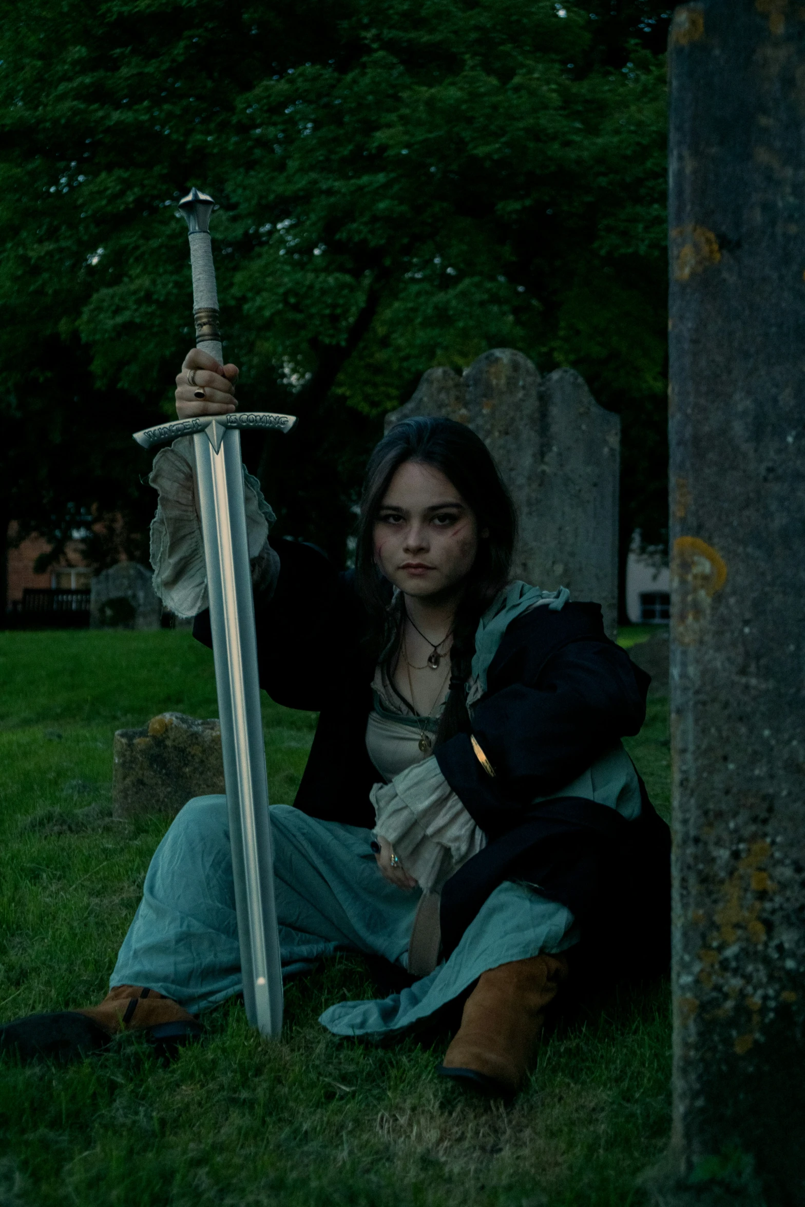 woman kneeling down holding a sword in front of a tombstone