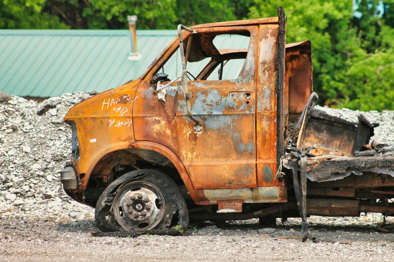 an old rusty, run down orange truck parked near a gravel pile