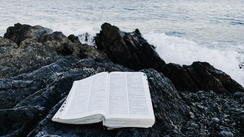 open book is sitting on a rock near the ocean