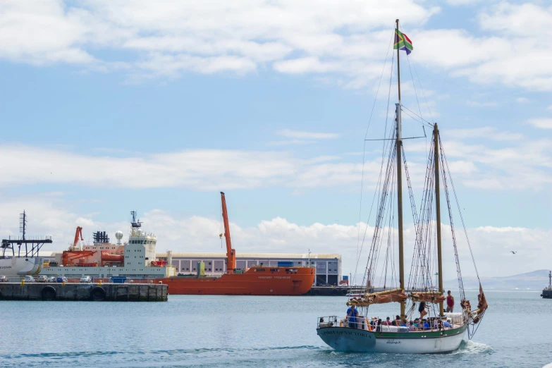 sailboat passing by several docked cargo vessels