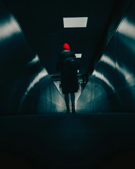 man standing in an otherwise dark tunnel with red beanie