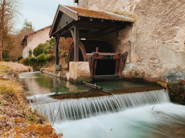 a watermill in front of a house next to the forest