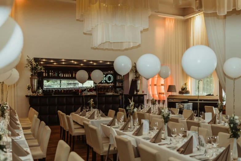 some white balloons are hanging over tables in a banquet room