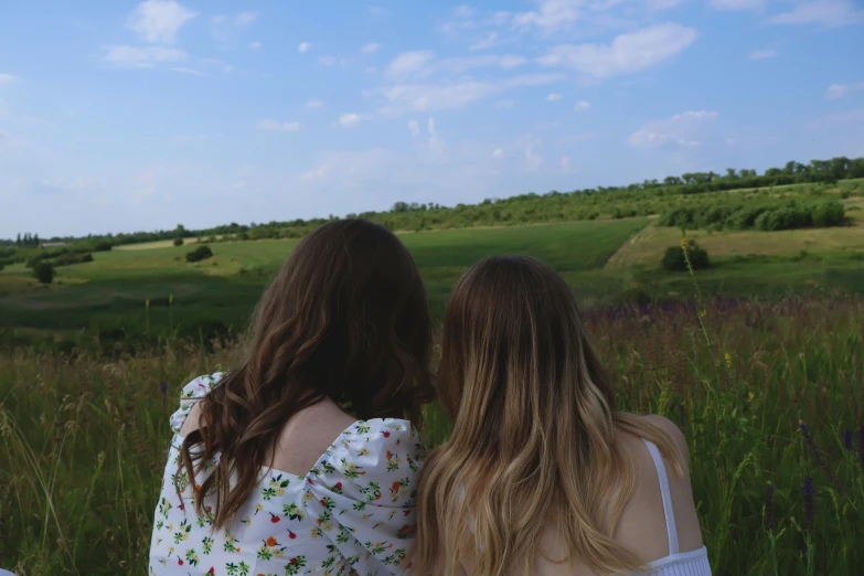 two women are sitting in a field watching the sky