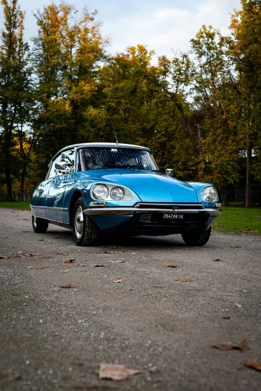 a small blue classic car parked on a gravel road