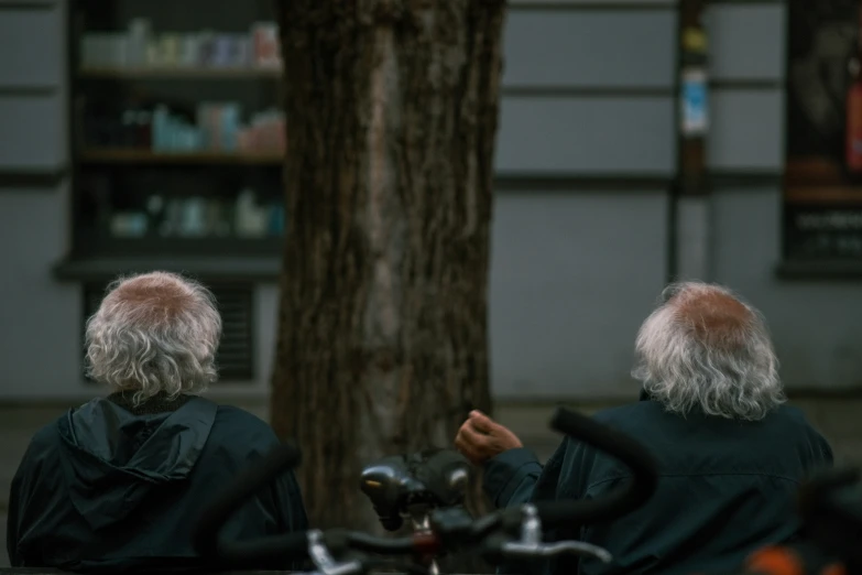 two people sitting next to a tree with a bicycle behind them