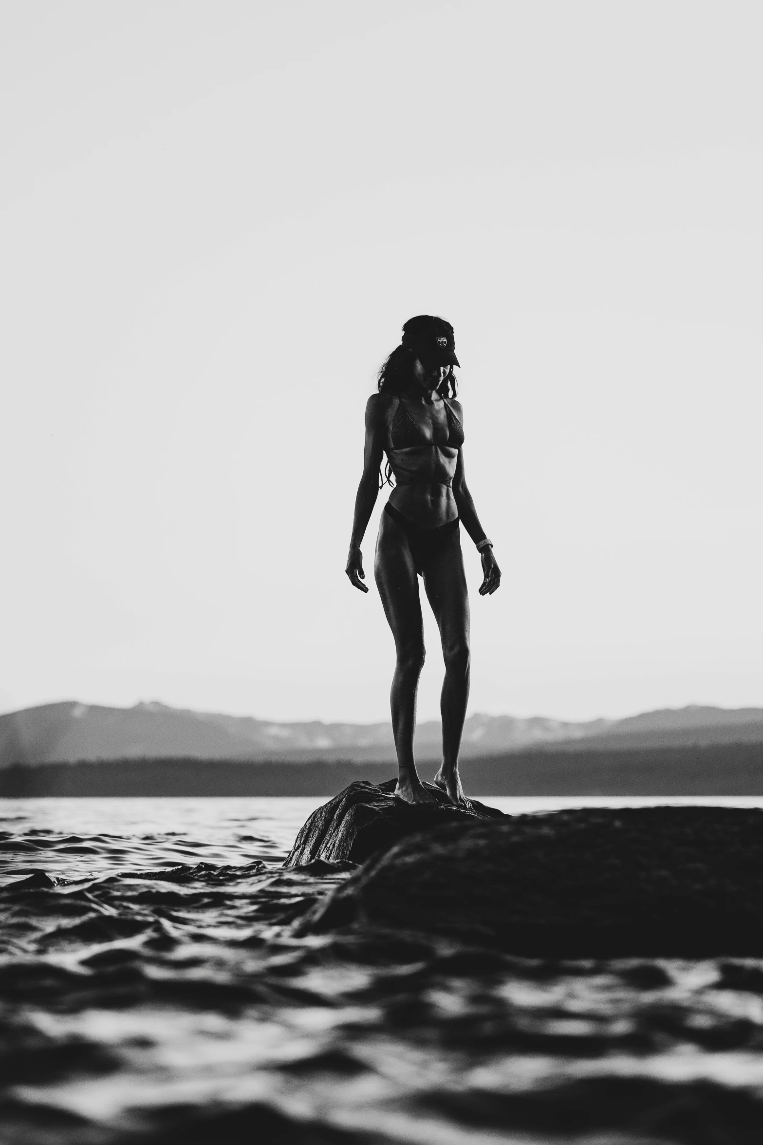 a woman in a bikini standing on the edge of a rock