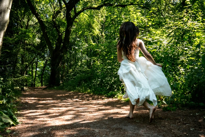 there is a woman wearing a white dress walking in the woods