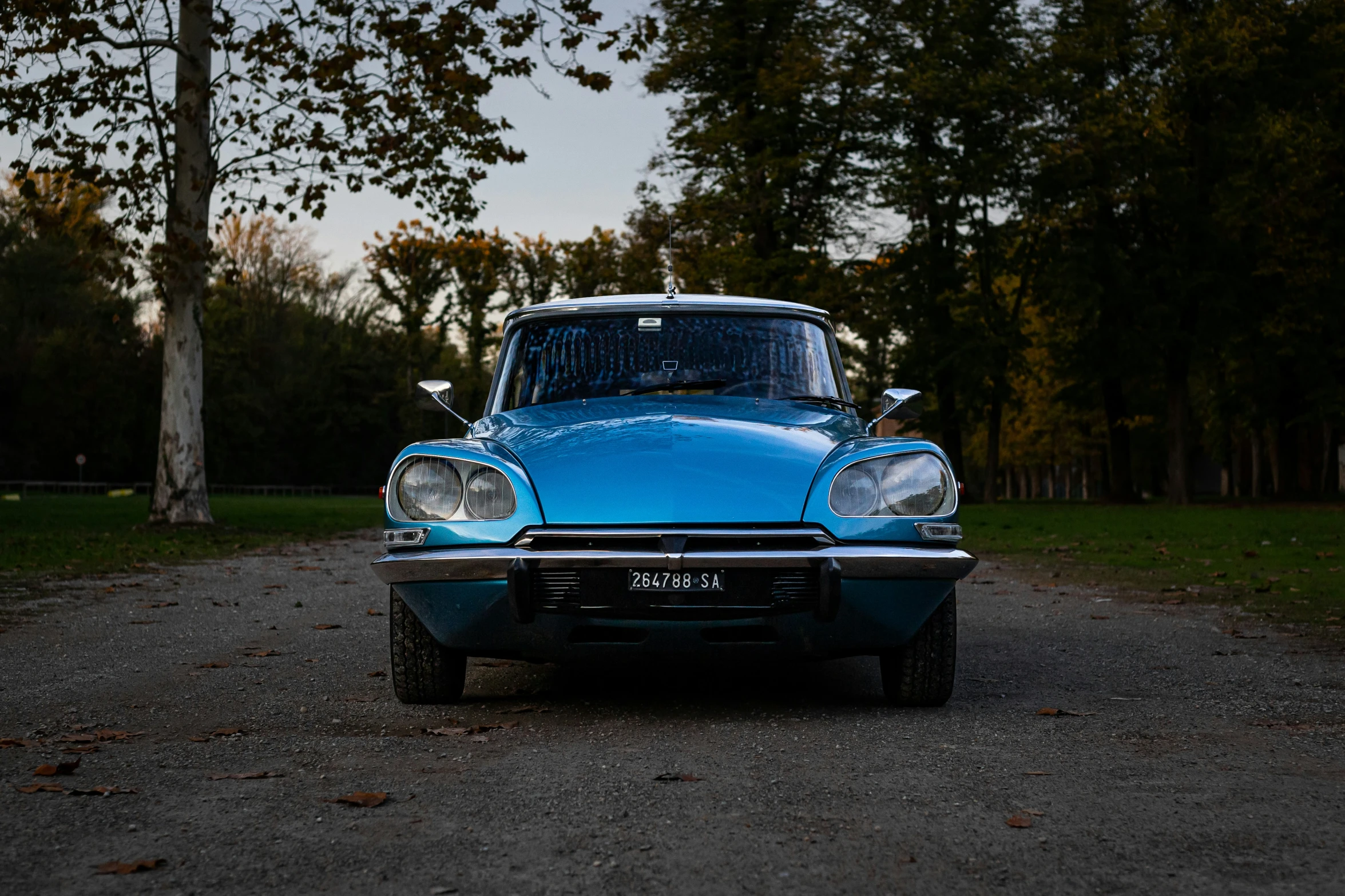 a blue old car parked on a dirt road near trees