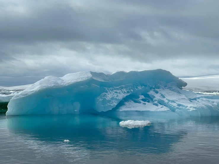 an iceberg with blue water and a very cloudy sky