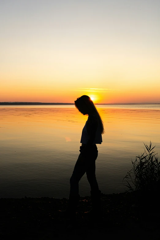 a woman walking along the shore of a lake at sunset