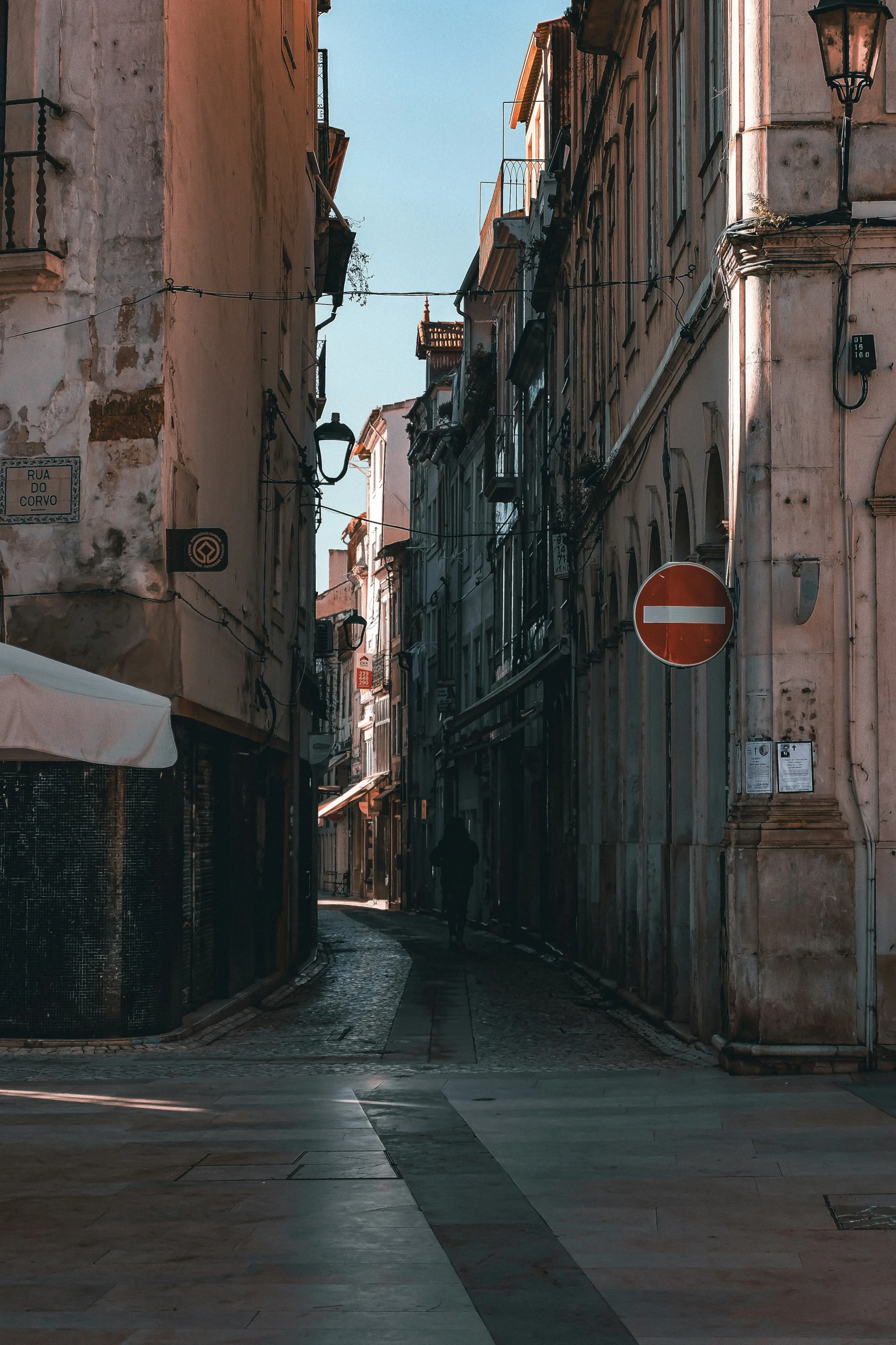 a narrow street that has cars and a clock on it