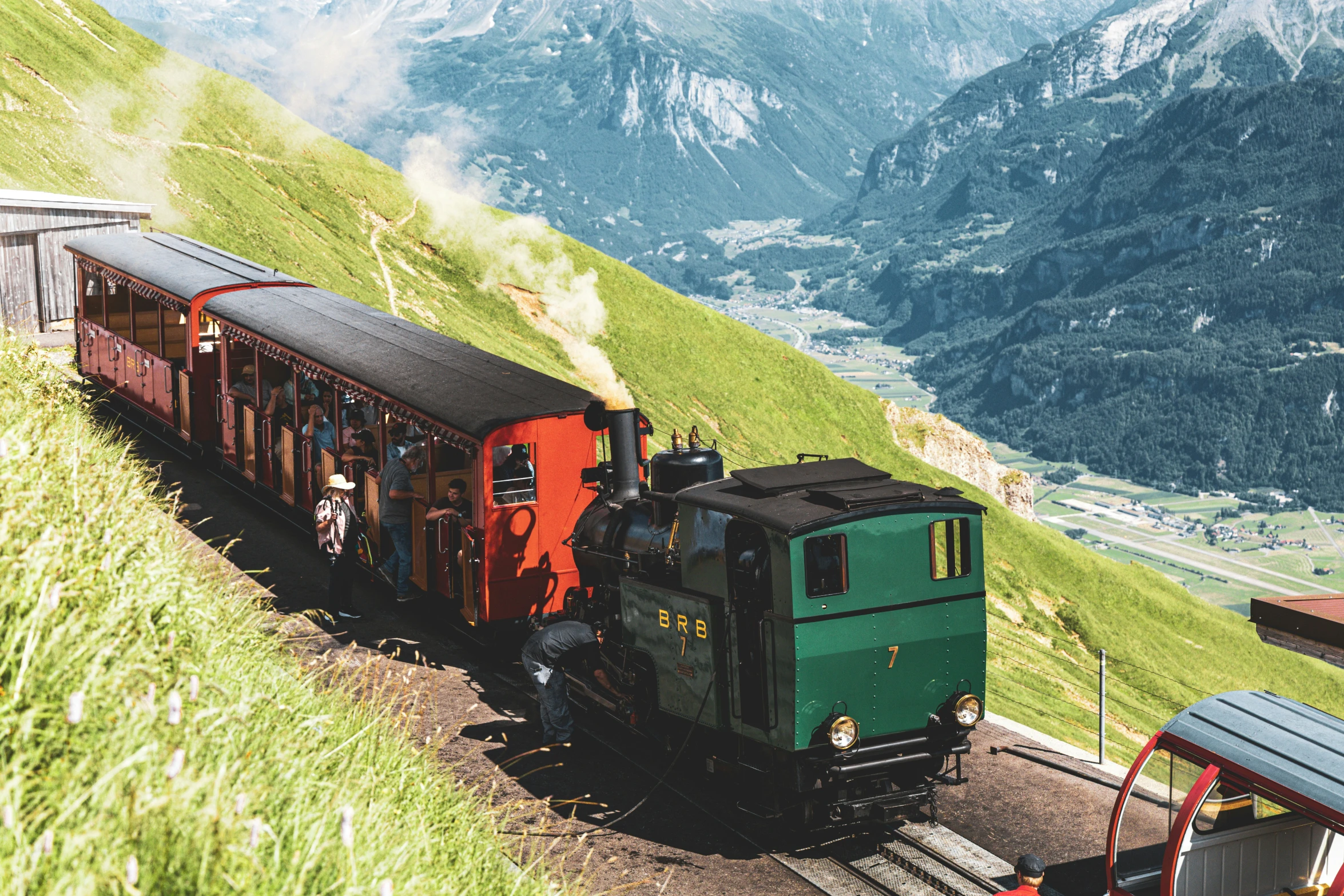 train passing by grass and mountains, with a small cabin next to it