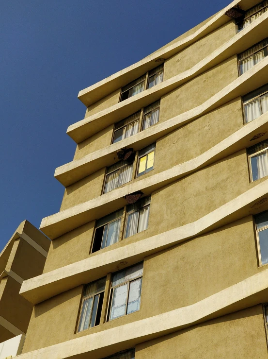 a tall yellow building has multiple windows and has a clock on it