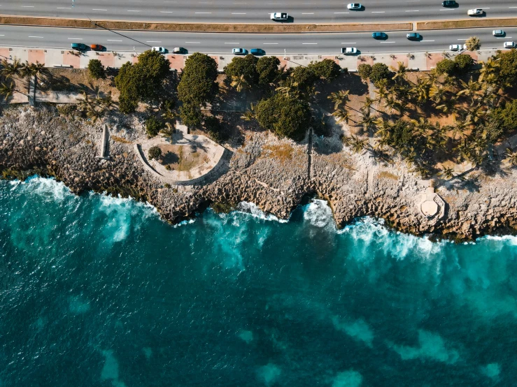 the ocean next to the beach has several cars driving by