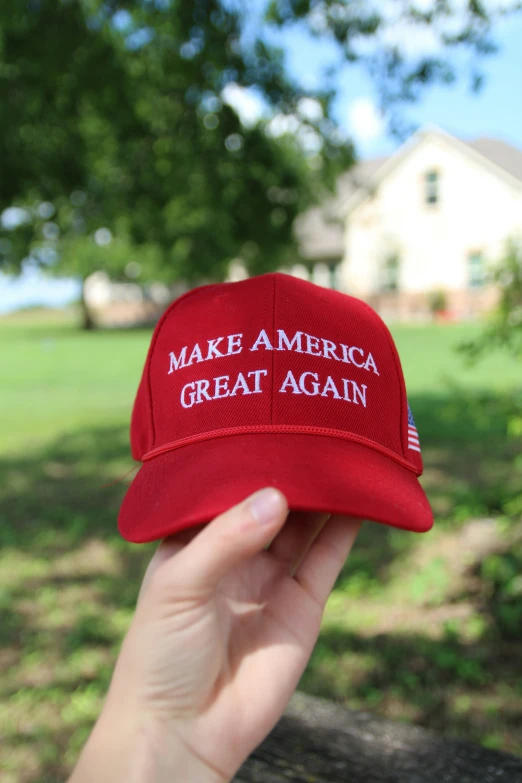 someone holding up a red hat with an american great again