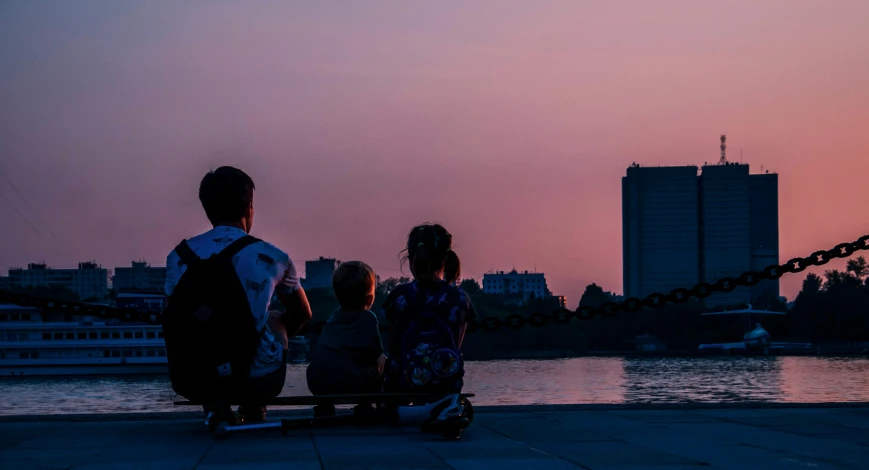 people sit on a bench near the water as the sun sets