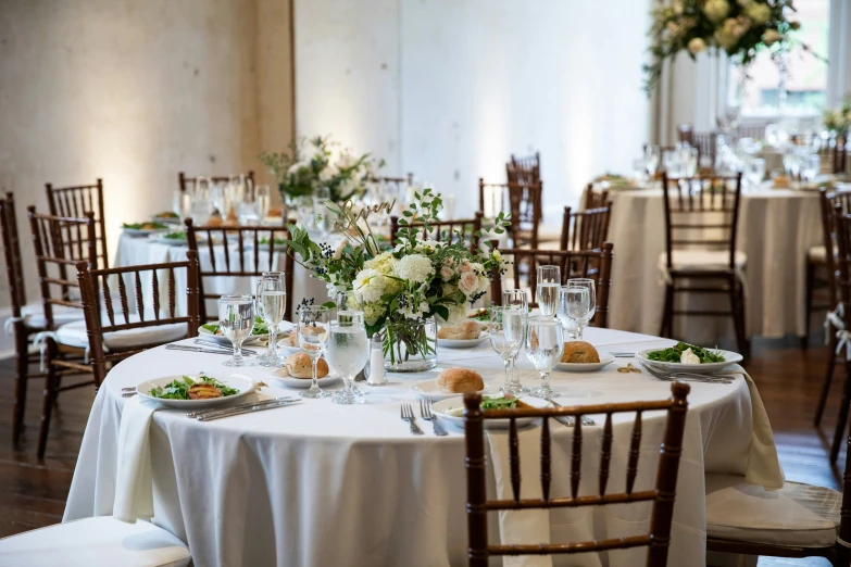 a table topped with a white clothed table and wooden chairs