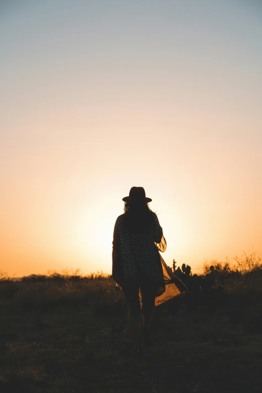 silhouette of a woman with flowers walking on a field at dusk