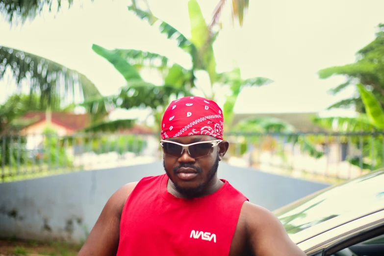 a man in red tank top with bandana standing next to a car