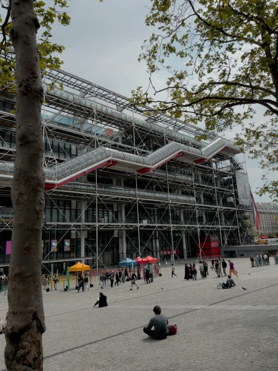 a building with scaffolding in front is under construction with people sitting on the ground