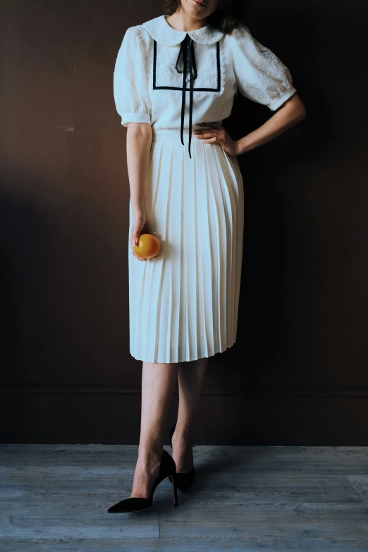 woman with hand on her hip and legs raised holding a peach, in front of a dark wall